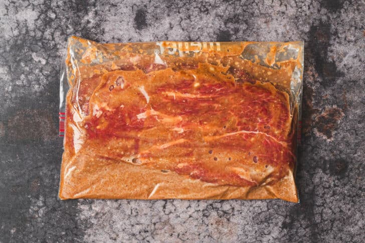 A zip top plastic bag filled with meat and flat iron steak marinade.