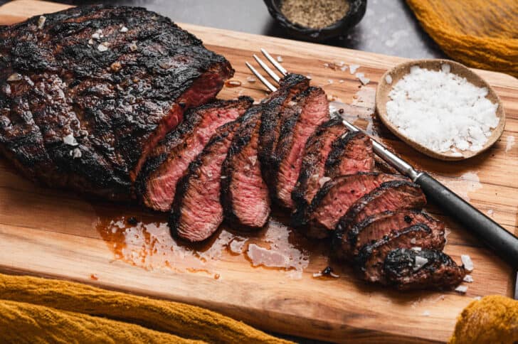 A flat iron steak thinly sliced on a cutting board.