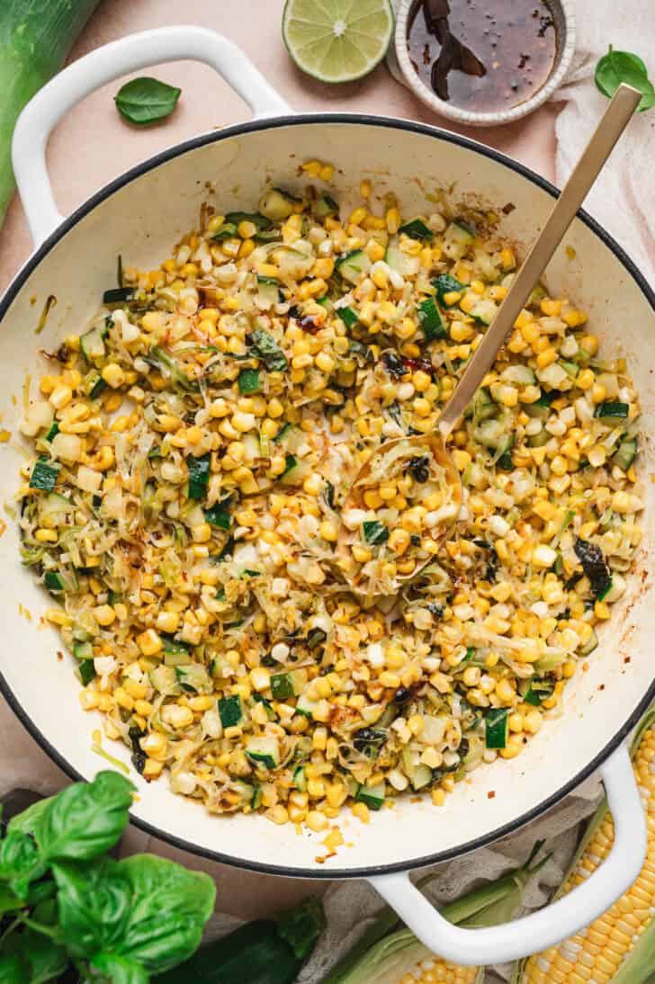 A white skillet with handles filled with a zucchini and corn recipe.