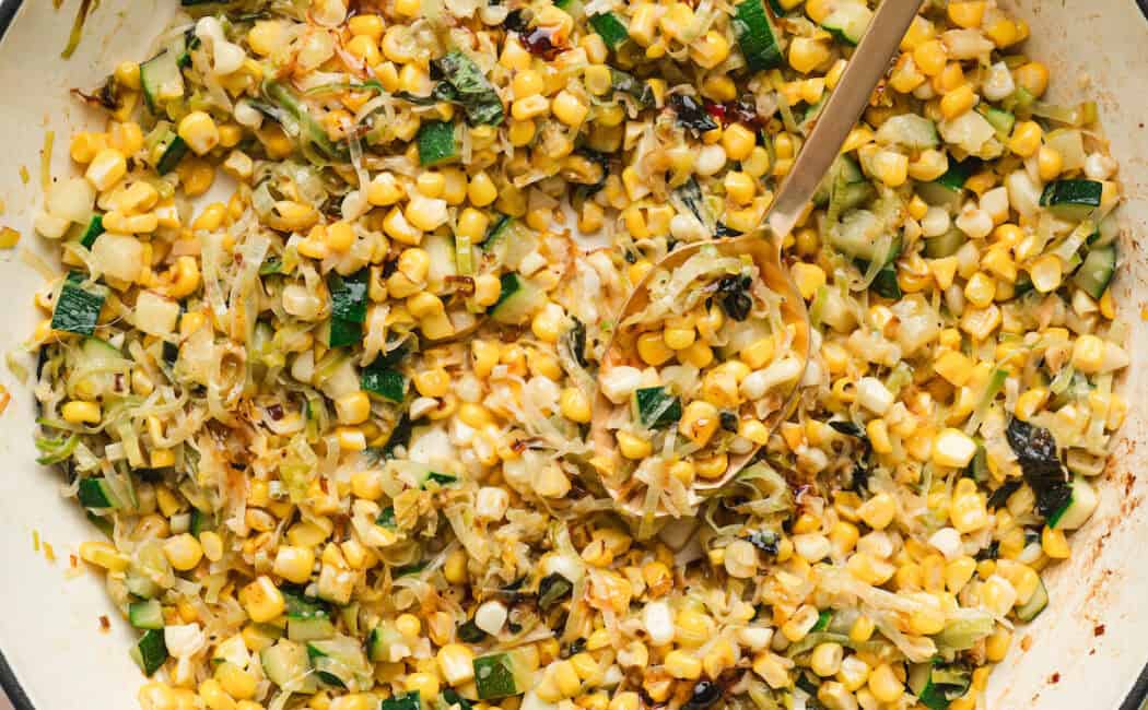 A white skillet with handles filled with a zucchini and corn recipe.