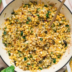 A white skillet with handles filled with a zucchini and corn recipe.