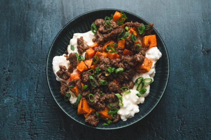 Overhead view of a sweet potato and turkey sausage cottage cheese bowl, topped with roasted sweet potatoes, turkey sausage crumbles, sliced green onions, and a drizzle of maple syrup.