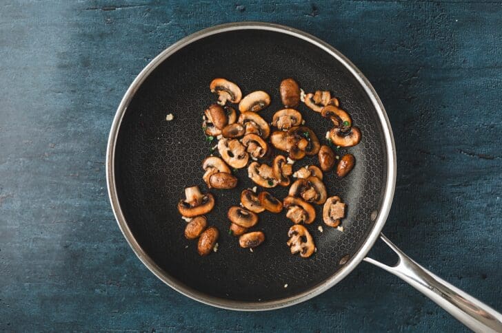 Overhead view of sliced mushrooms sautéing in a skillet until browned.