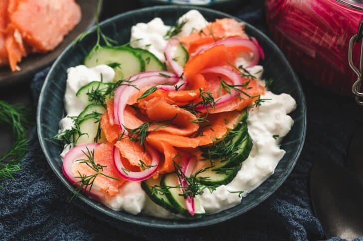 Overhead view of a smoked salmon and dill cottage cheese bowl, topped with sliced cucumbers, pickled red onions, and fresh dill.