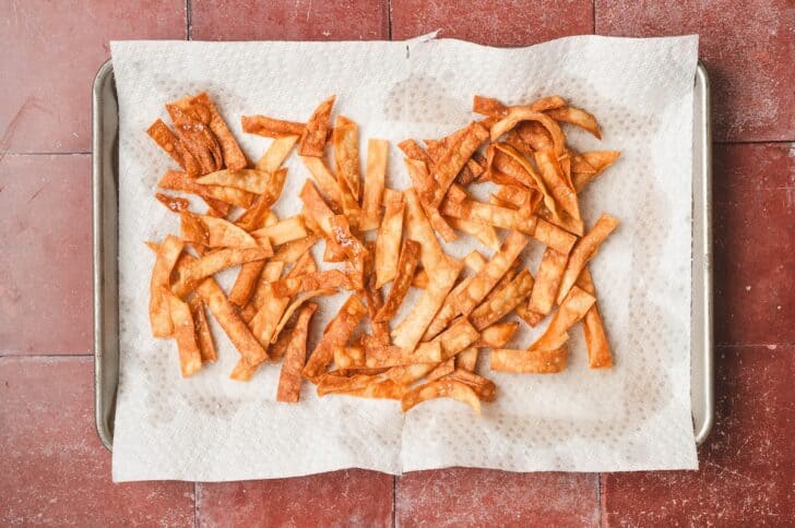 Overhead view of freshly fried tortilla strips draining on paper towels on a baking sheet.