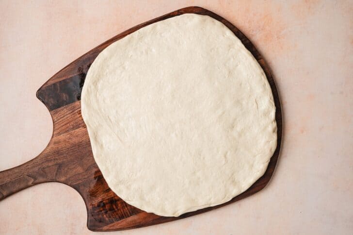 Overhead view of stretched pizza dough on a wooden pizza peel, ready to be topped.