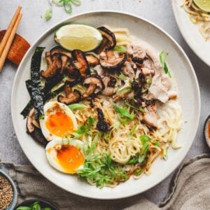 Overhead view of a bowl of creamy chicken ramen garnished with shiitake mushrooms, soft-boiled egg, nori, and a lime wedge
