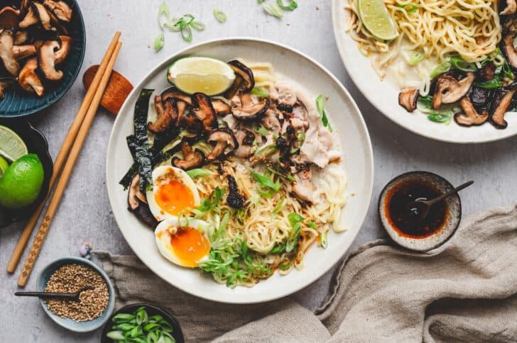 Two bowls of creamy ramen recipe with chicken, mushrooms, soft-boiled eggs, and a side of chili crisp for topping