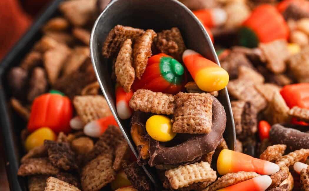Scoop lifting halloween chex mix loaded with candy corn, mellowcreme pumpkins, chocolate-covered pretzels, and Reese's Pieces