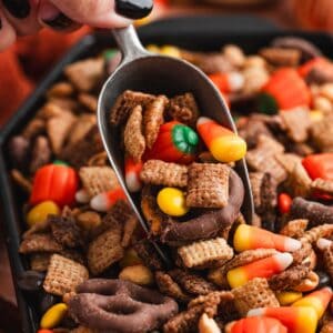 Scoop lifting halloween chex mix loaded with candy corn, mellowcreme pumpkins, chocolate-covered pretzels, and Reese's Pieces