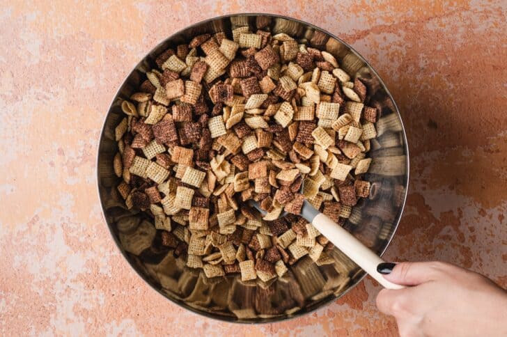 Overhead shot of cinnamon and chocolate Chex cereal being stirred together in a large bowl for halloween party mix