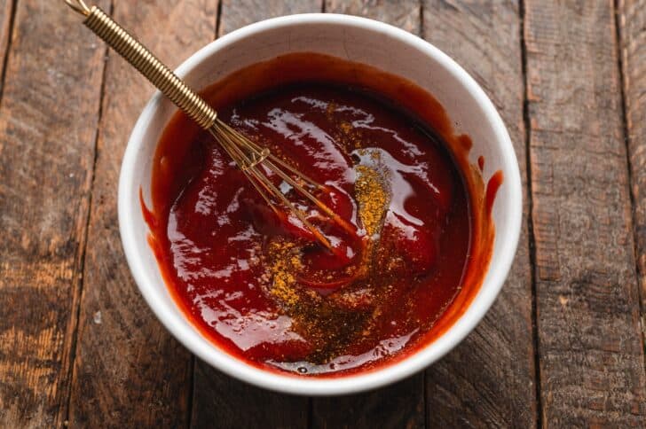 Curry powder being whisked into ketchup for the curry dipping sauce that goes with halloween pigs in a blanket