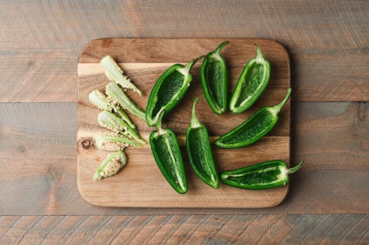 Overhead view of jalapeño peppers halved lengthwise and seeded, arranged on a wooden cutting board.