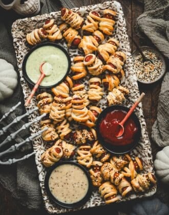 Overhead platter of lil smokies pigs in a blanket arranged with dipping sauces, a ceramic skull, and a skeleton hand