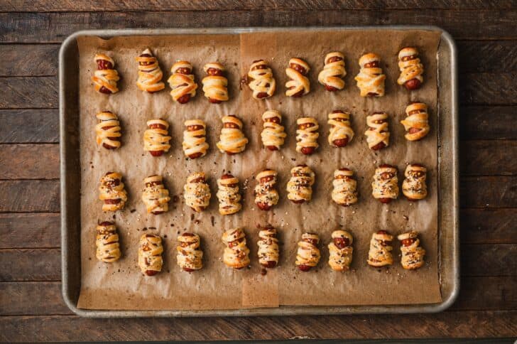 Unbaked little smokies pigs in a blanket lined up in rows on a parchment-lined baking sheet