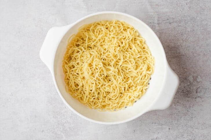 Cooked ramen noodles draining in a white colander before being added to bowls