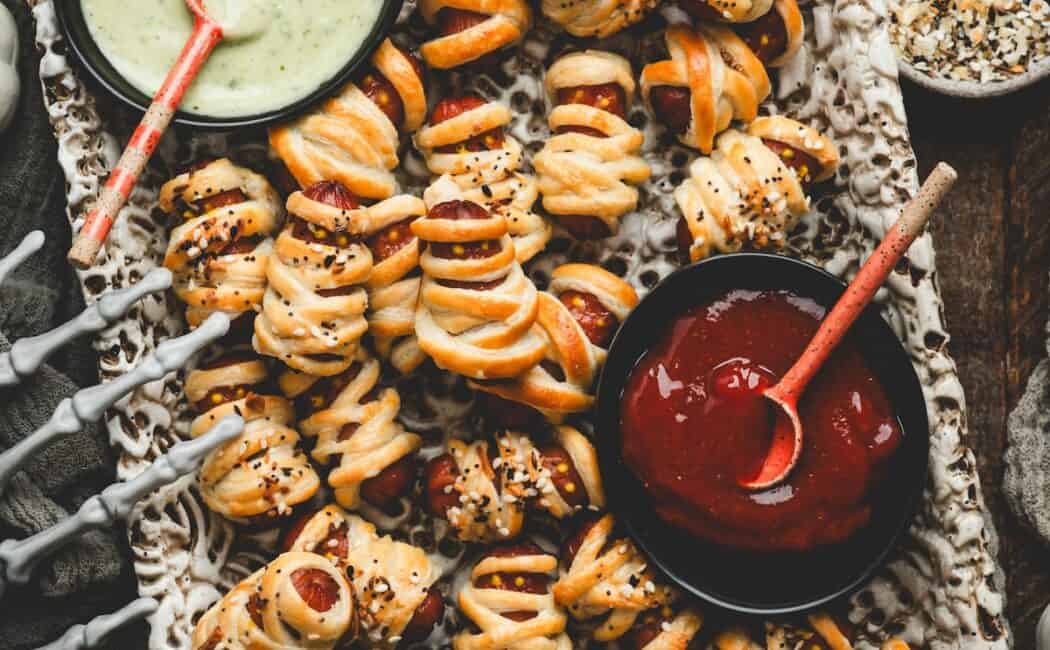 Close crop of a platter of mummy pigs in a blanket surrounded by dipping sauces and Halloween decor