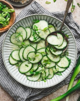 Overhead bowl of asian cucumber salad tossed in a rice vinegar dressing with scallions and sesame seeds, served with a spoon