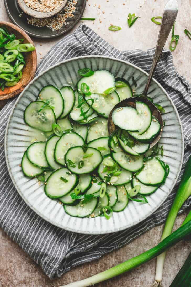 Overhead bowl of asian cucumber salad tossed in a rice vinegar dressing with scallions and sesame seeds, served with a spoon