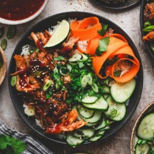 Asian pulled pork rice bowl with cucumber salad, carrot ribbons, cilantro, green onions and sesame seeds