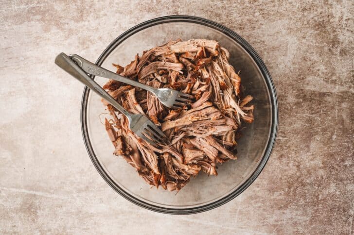 Tender slow-cooked pork shredded with two forks in a large glass bowl