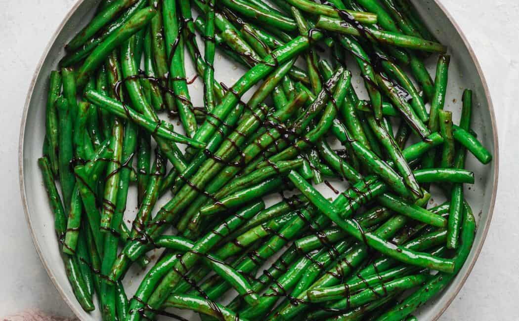 Overhead view of balsamic green beans in a skillet, crisscrossed with a dark balsamic drizzle