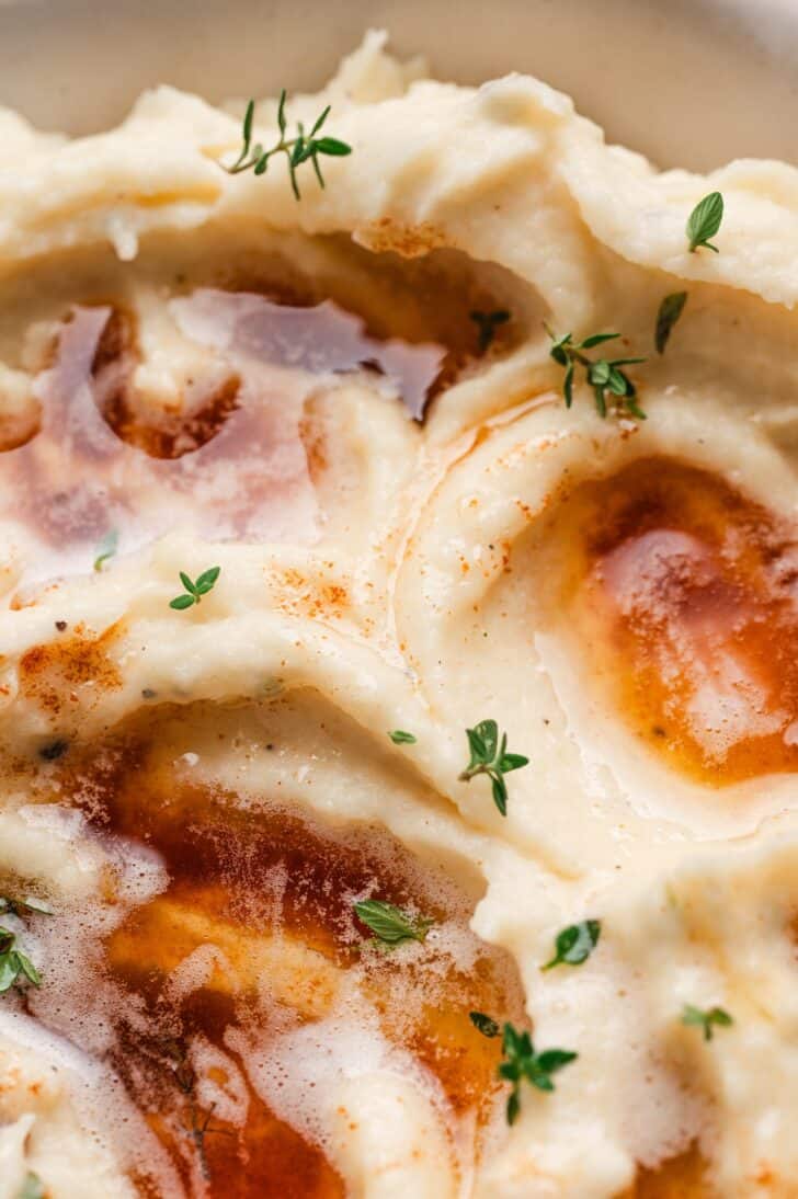 Extreme close-up of browned butter drizzled over mashed parsnips, with golden-brown milk solids and fresh thyme leaves scattered on top