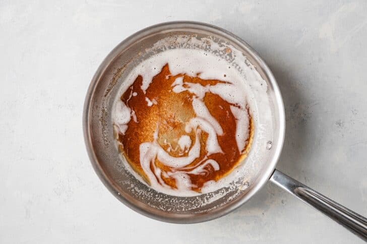 Close overhead crop of browned butter in a skillet, its golden-brown milk solids swirled through melted foam