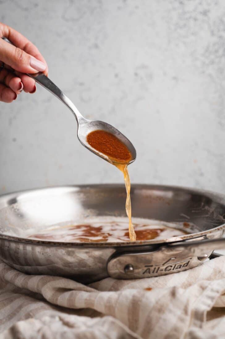 A hand tilting a spoonful of brown butter back into the skillet, demonstrating how to brown butter at the final toasted stage