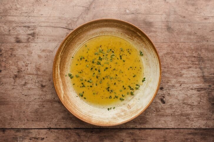 Overhead shot of maple-mustard vinaigrette whisked together in a bowl, flecked with fresh thyme