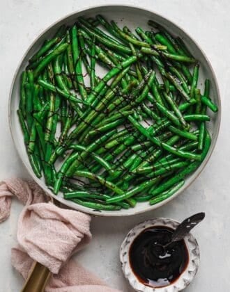 Overhead view of balsamic green beans in a skillet, crisscrossed with a dark balsamic drizzle