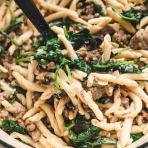 Scoop lifting strozzapreti pasta with crumbled Italian sausage, wilted kale and spinach from the pot, one of our favorite ground italian sausage recipes