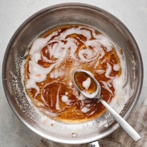 Overhead shot of a brown butter recipe in a stainless steel skillet, with deep amber milk solids swirled through the foam and a spoon resting in the pan