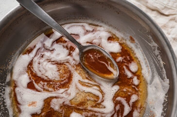 Close-up of a spoon resting in a skillet of beurre noisette, its deep amber milk solids visible beneath the foam