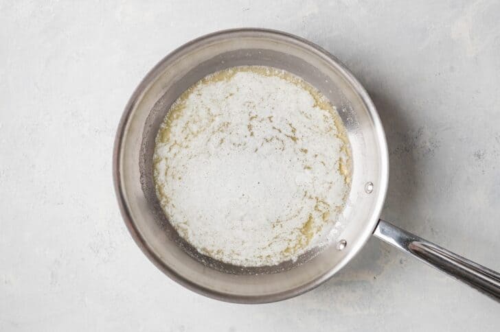 Overhead shot of butter foaming in a skillet, held over the stove as it just begins to melt