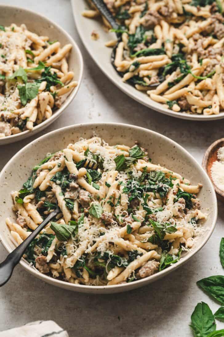 Three bowls of italian sausage pasta topped with grated Parmesan and fresh basil