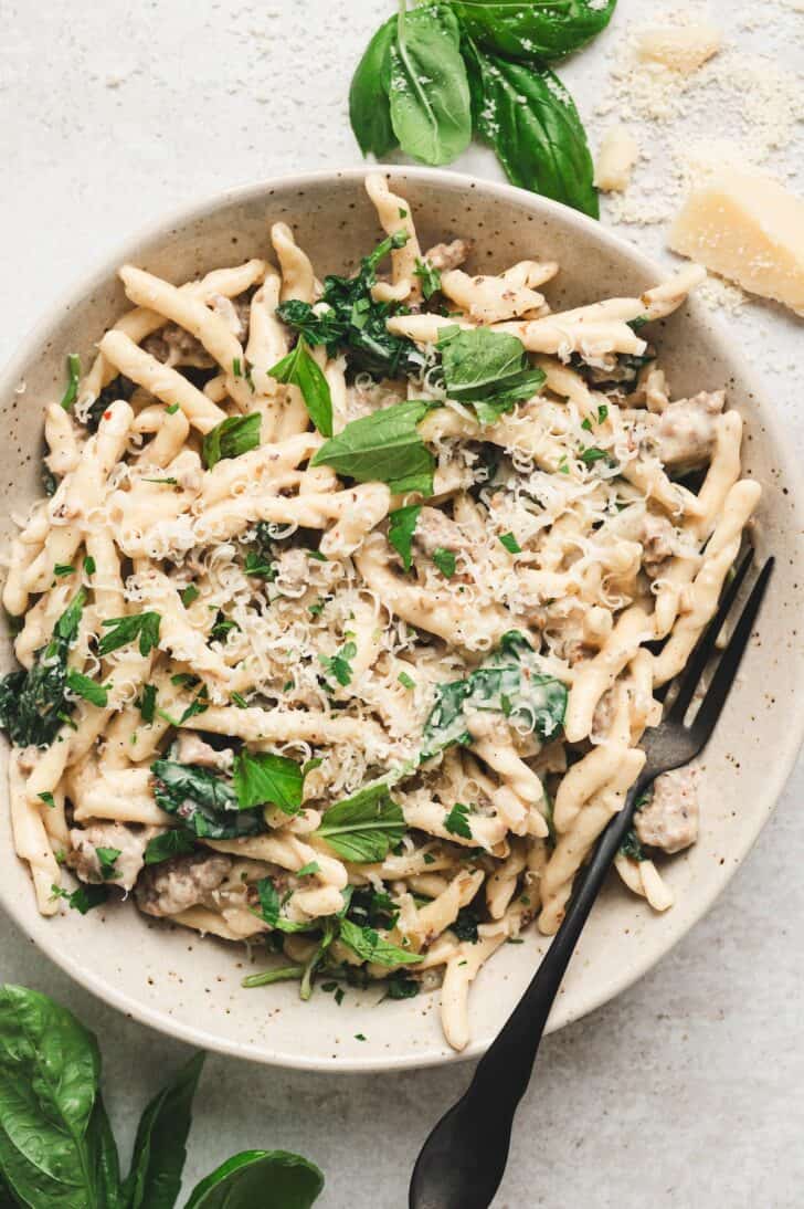 Overhead bowl of italian sausage pasta recipes topped with grated Parmesan, fresh basil, and parsley