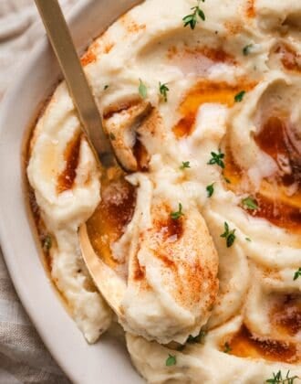 Close-up of a spoon digging into a bowl of mashed parsnips topped with brown butter and fresh thyme leaves