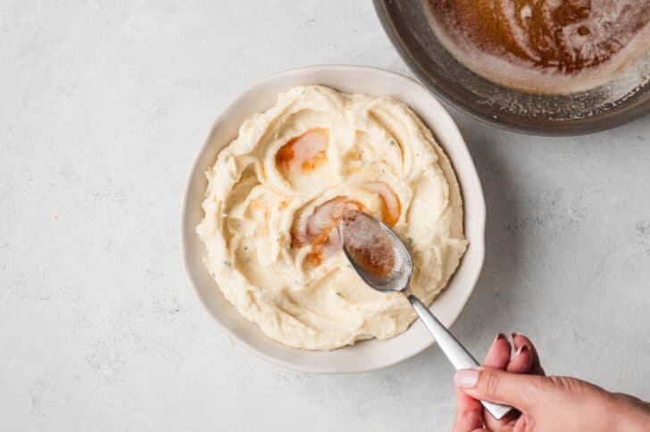 A spoon drizzling warm brown butter into a shallow well in the center of a bowl of puree
