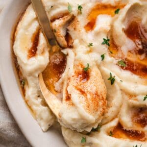 Close-up of a spoon digging into a bowl of mashed parsnips topped with brown butter and fresh thyme leaves