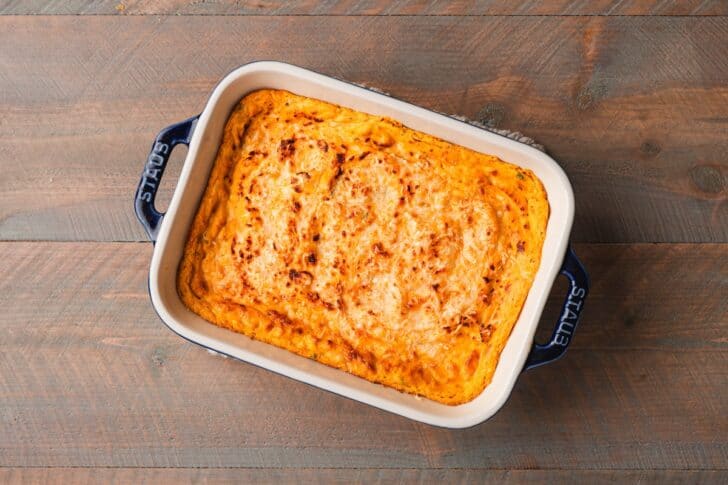 Overhead view of a savory pumpkin dip baked until browned and bubbly in a blue ceramic baking dish