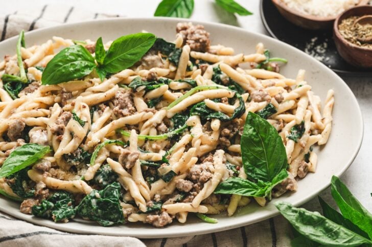 Platter of pasta with crumbled sausage and wilted greens garnished with fresh basil, one of our favorite recipes with italian sausage