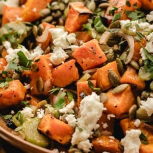 Extreme close-up of sweet potato salad with feta cheese, roasted pumpkin seeds, sliced shallot, and chopped parsley