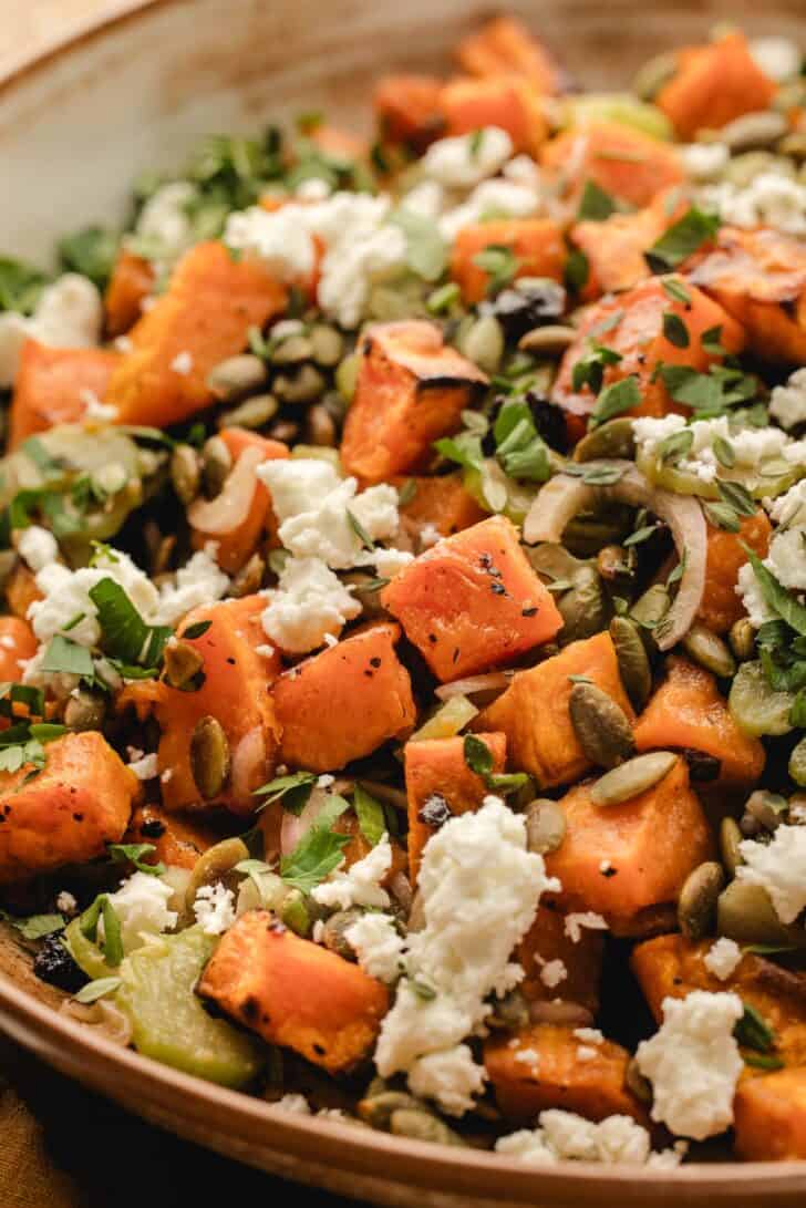 Close angled shot of warm sweet potato salad with two forks digging in, showing roasted sweet potatoes, celery, dried cherries, and feta