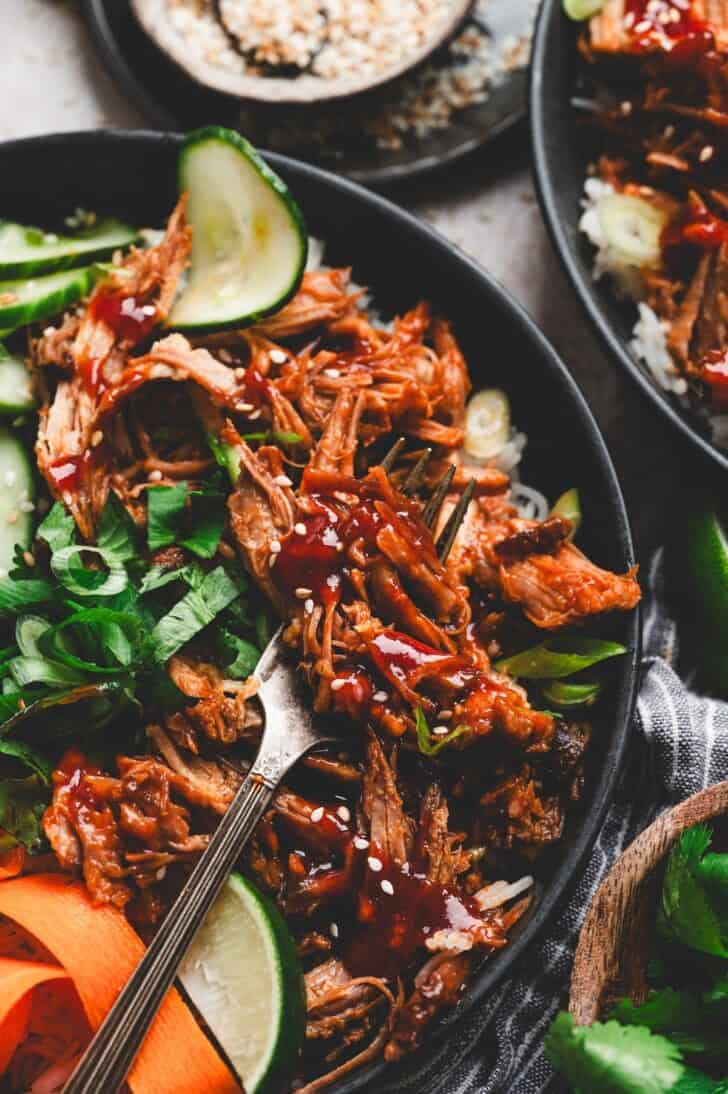 Forkful of slow cooker Asian pork with BBQ sauce, rice, cucumber, cilantro and sesame seeds