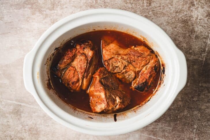 Slow-cooked pork shoulder chunks sitting in cooking juices before being shredded