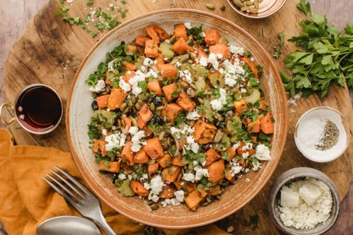 Overhead view of fall sweet potato salad served in a rustic bowl, styled with fresh parsley, and small bowls of salt and feta