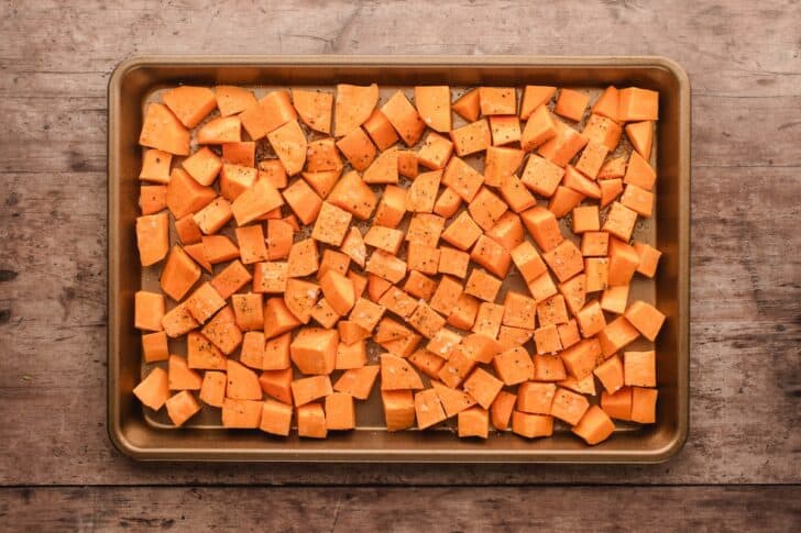 Cubed raw sweet potatoes spread on a rimmed baking pan