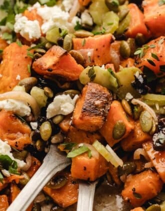 Extreme close-up of feta sweet potato salad with two forks lifting a bite, showing roasted sweet potato cubes, celery, and dried cherries