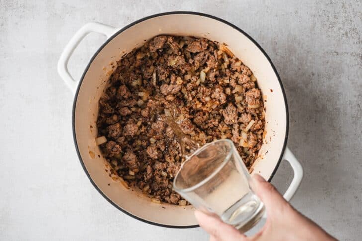 Process shot of white wine being poured into browned ground sausage and onion to deglaze the pot